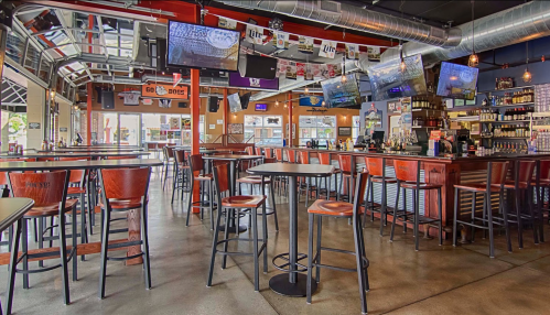 A spacious bar area with high tables and stools, large TVs, and a vibrant atmosphere, ready for patrons.