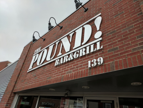 Sign for "The Pound! Bar & Grill" on a brick building, featuring bold white letters and a street number of 139.