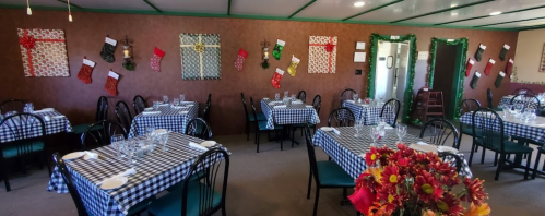 Cozy dining area with checkered tablecloths, festive decorations, and holiday stockings on the walls.