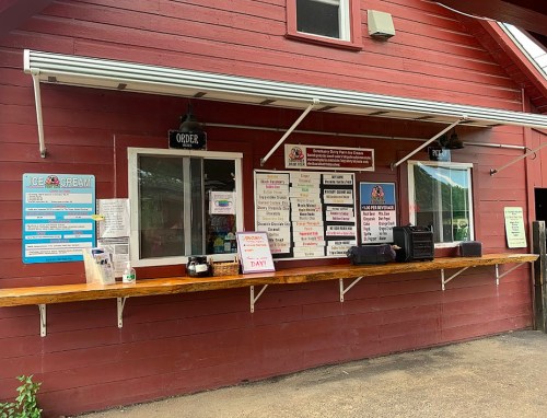 A red wooden building with an outdoor service window displaying a menu and ice cream options.
