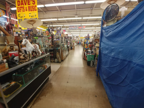 A wide aisle in a cluttered store filled with various items, displays, and a blue tarp on the right side.