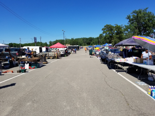 A bustling outdoor market with vendors under colorful tents, showcasing various goods along a wide, paved pathway.