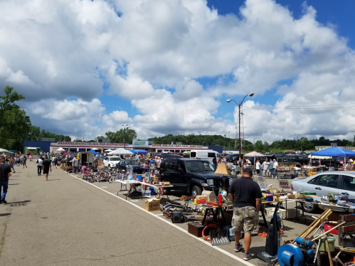 A bustling flea market with various stalls, shoppers browsing, and a cloudy sky overhead.