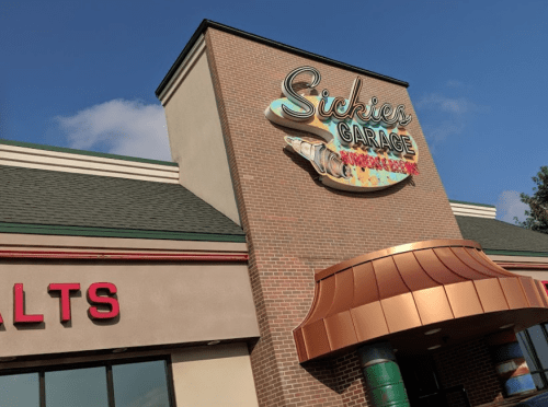 Sign for Sickies Garage, a restaurant, featuring colorful lettering and a fish design on a brick building.