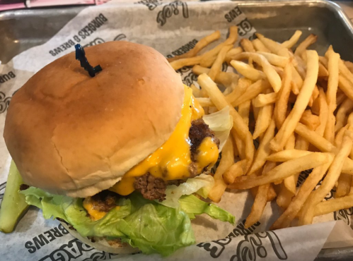 A cheeseburger with lettuce and a pickle, served with a side of golden French fries on a metal tray.