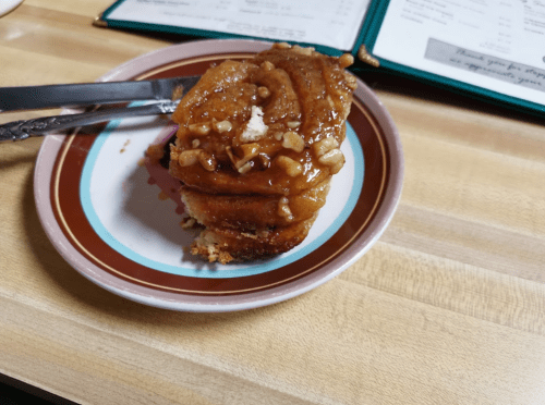 A slice of sticky caramel pecan coffee cake on a plate, with a fork and knife beside it.