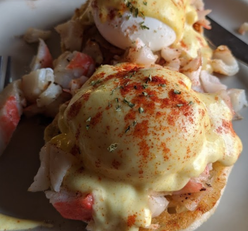 Close-up of eggs Benedict topped with hollandaise sauce, crab meat, and paprika on an English muffin.