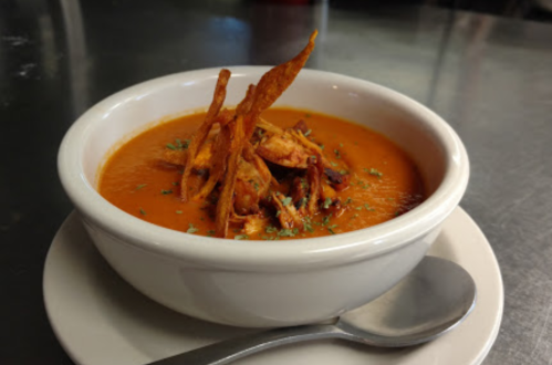 A bowl of creamy soup topped with crispy fried strips and herbs, served on a white plate with a spoon.