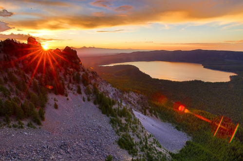 Sunset over a lake, with vibrant colors illuminating the sky and rocky terrain in the foreground.