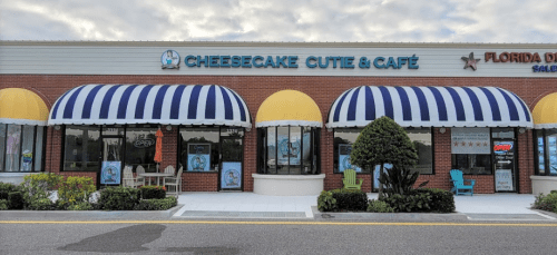 Exterior of Cheesecake Cutie & Café with yellow and blue striped awnings, featuring a welcoming entrance and outdoor seating.