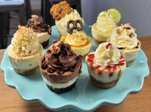 A colorful assortment of mini cheesecakes topped with various decorations on a teal cake stand.
