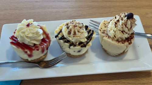 Three mini cheesecakes on a plate: one with strawberry topping, one with chocolate drizzle, and one with cocoa powder.