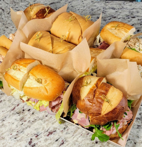 A variety of sandwiches in a takeout box, featuring different breads and fillings, arranged on a marble countertop.