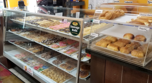 A display case filled with various donuts and pastries, including sausage rolls, croissants, and cheese danishes.