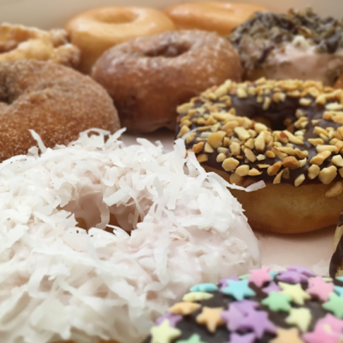 A variety of colorful donuts, including coconut, chocolate, and sprinkles, arranged on a light background.