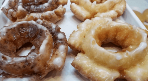 A close-up of glazed donuts in various flavors, showcasing a mix of light and dark icing on a white plate.