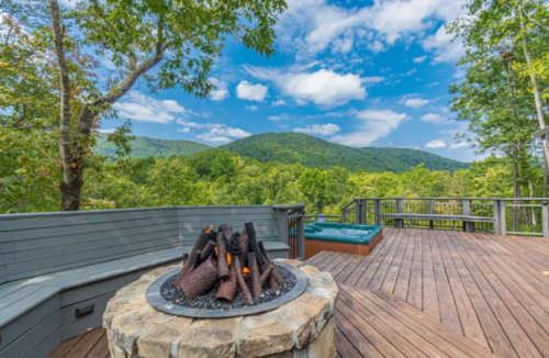 A scenic deck with a fire pit, surrounded by lush green mountains and a clear blue sky.