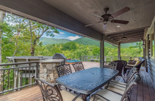 A spacious outdoor patio with a dining table, surrounded by trees and mountains in the background.