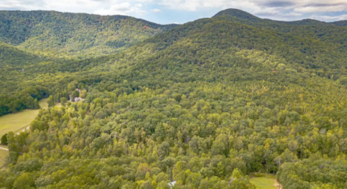 Aerial view of lush green mountains and dense forest under a partly cloudy sky.