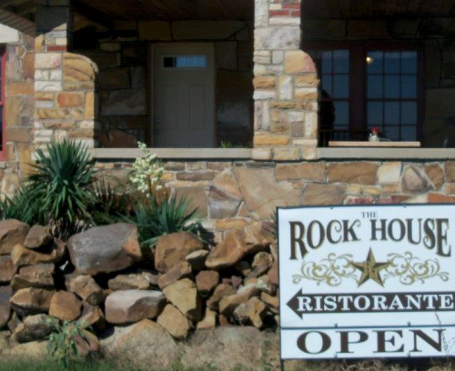 A stone building with a sign reading "The Rock House Ristorante Open" and greenery in front.