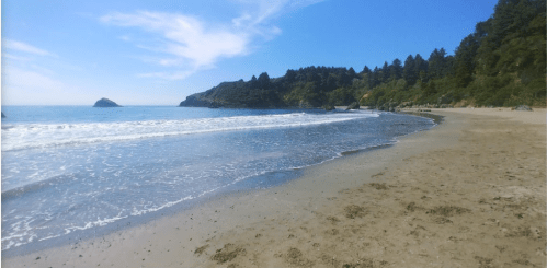 A serene beach scene with gentle waves, sandy shore, and lush green hills under a clear blue sky.