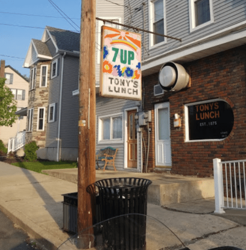 Sign for Tony's Lunch with a colorful 7UP logo, in front of a two-story building on a sunny day.