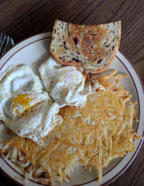 A plate with two fried eggs, crispy hash browns, and a slice of toasted bread.