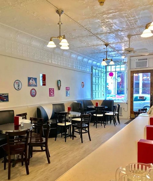 A cozy diner interior with black chairs, round tables, and vintage decor, featuring a bright, welcoming atmosphere.