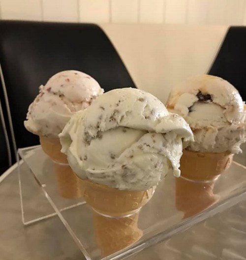 Three ice cream cones in a clear display, featuring flavors of pink, white, and beige ice cream.