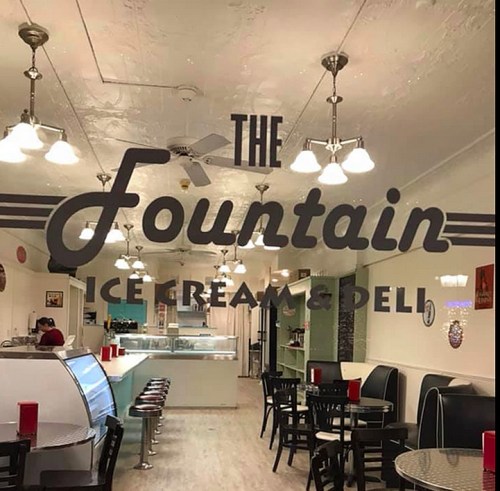 Interior of "The Fountain" ice cream and deli, featuring retro decor, tables, and a display case.