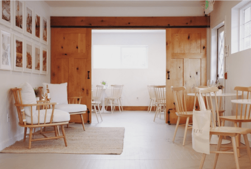 A cozy, minimalist café with wooden furniture, light walls, and framed photos on the wall.