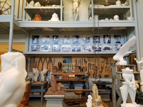 A workshop filled with sculptures, tools, and photographs on the walls, showcasing an artistic environment.