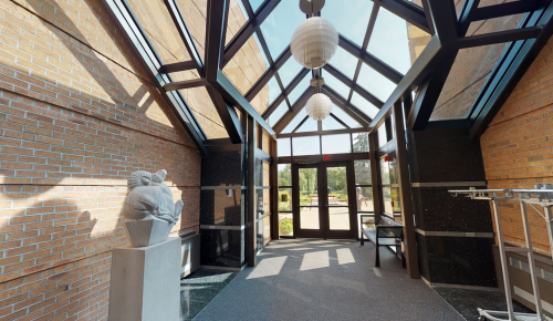 Bright entryway with large windows, a sculpture on a pedestal, and modern lighting fixtures.
