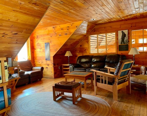 Cozy wooden living room with leather sofas, a coffee table, and large windows, featuring warm, natural lighting.