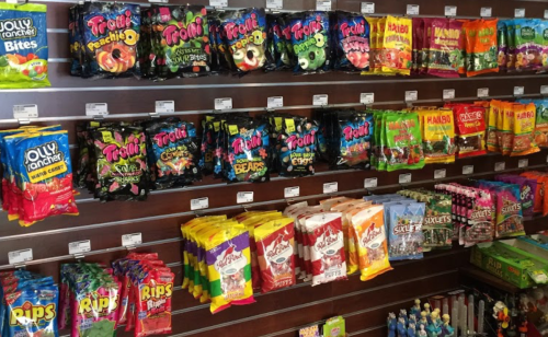 A colorful display of various candy bags on shelves, including Trolli, Jolly Rancher, and Skittles.