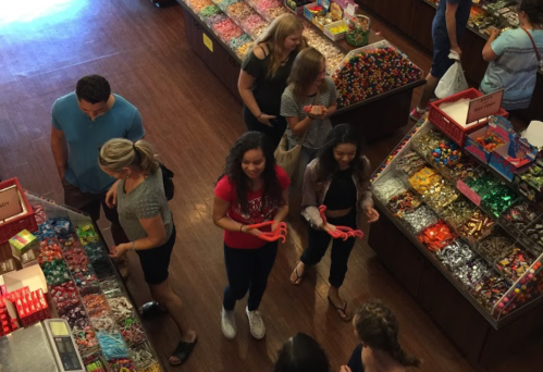 A colorful candy store filled with people selecting sweets from various displays.