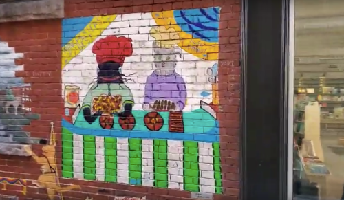 Colorful mural depicting two chefs with various dishes on a table, set against a brick wall.