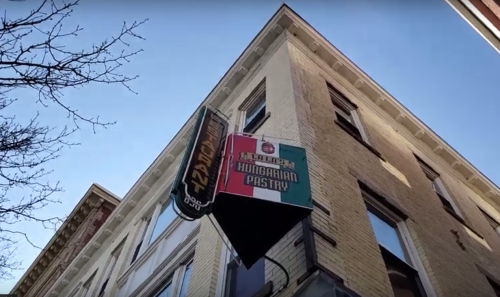 Sign for a Hungarian pastry shop on a building, with a clear blue sky in the background.