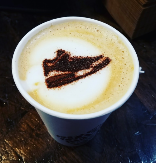 A coffee cup with frothy milk topped with a chocolate design of a sneaker.