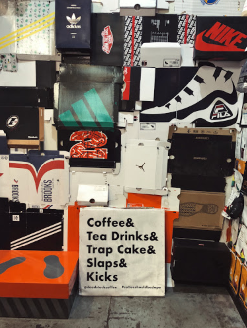 A wall covered in various sneaker boxes with a sign promoting coffee, tea, and snacks.
