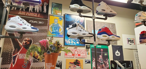 A display of sneakers hanging on pipes, surrounded by sports posters and a colorful flower arrangement.