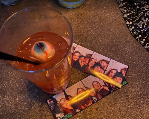 A cocktail with a garnish and photo strips of friends laughing on a table.