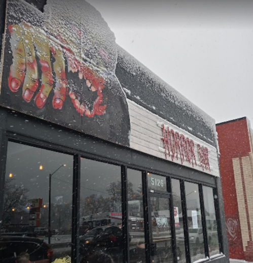 A snowy scene of a restaurant exterior featuring a large, colorful mural of a hand on the wall.