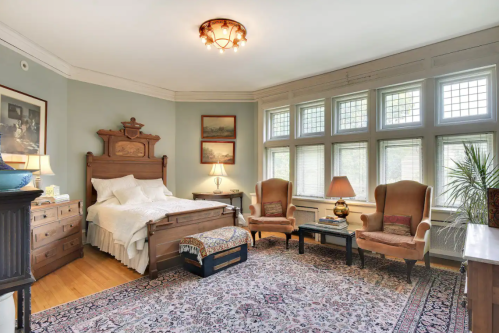 Cozy bedroom featuring a wooden bed, armchairs, a rug, and large windows with natural light.