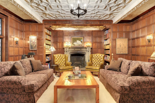 Cozy library with wooden paneling, plush sofas, a fireplace, and elegant decor, creating a warm, inviting atmosphere.
