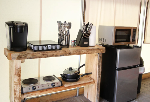 A rustic kitchen setup featuring a coffee maker, cookware, a microwave, and a mini fridge on a wooden shelf.