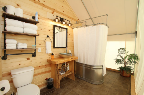 A rustic bathroom with wooden walls, a shower curtain, sink, towels, and a potted plant in the corner.
