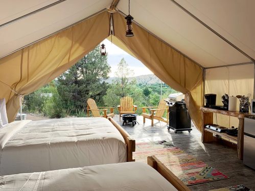 Cozy glamping tent with two beds, a kitchenette, and outdoor seating overlooking a scenic landscape.
