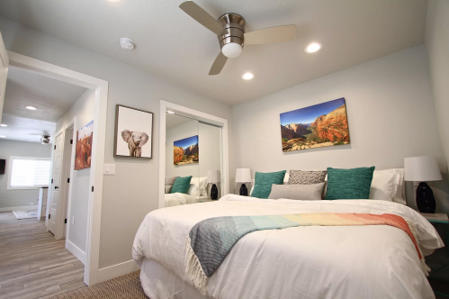 Cozy bedroom with a large bed, decorative pillows, a ceiling fan, and artwork on the walls. Bright and inviting space.