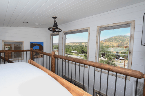 Interior view of a room with wooden railing, large windows showcasing a scenic mountain landscape outside.
